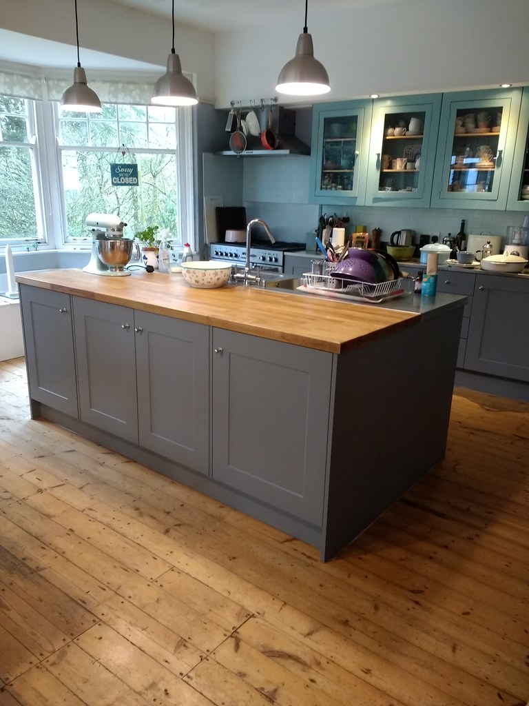 Fitted kitchen with grey island unit, oak worktop, and pendant lights installed by Greener Building