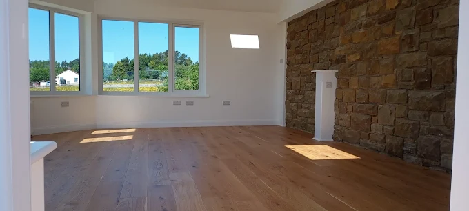 New build interior with oak flooring, exposed stone feature wall, and large windows overlooking the countryside